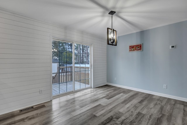 unfurnished dining area featuring hardwood / wood-style flooring, wooden walls, crown molding, and an inviting chandelier