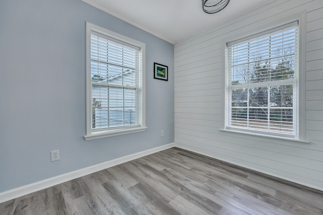 unfurnished room featuring ornamental molding, wooden walls, and light wood-type flooring