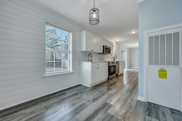 kitchen with sink, light hardwood / wood-style flooring, pendant lighting, stainless steel appliances, and white cabinets