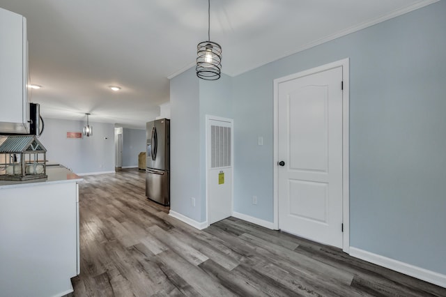 kitchen with hanging light fixtures, ornamental molding, appliances with stainless steel finishes, hardwood / wood-style floors, and white cabinets