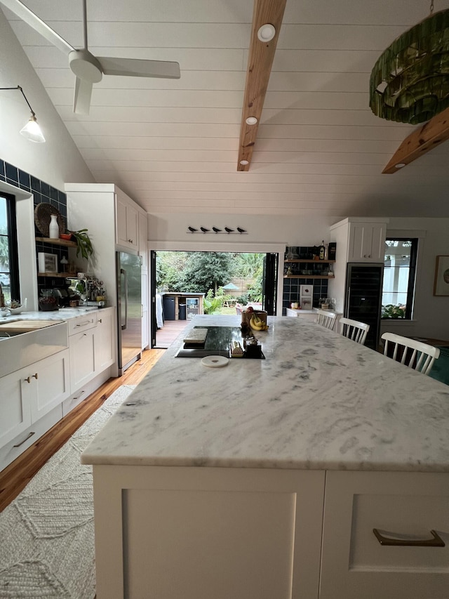 kitchen with white cabinets, lofted ceiling with beams, stainless steel fridge, and light stone counters