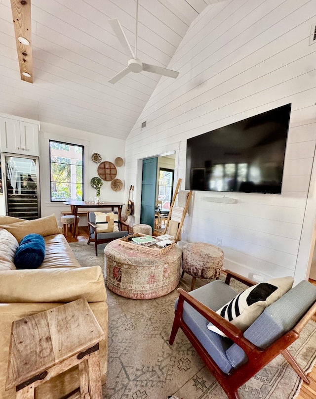 living room featuring ceiling fan, wood-type flooring, wooden walls, and high vaulted ceiling