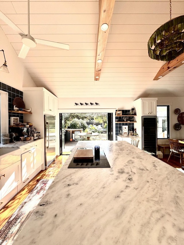 kitchen featuring decorative light fixtures, black electric stovetop, beamed ceiling, high end fridge, and white cabinets