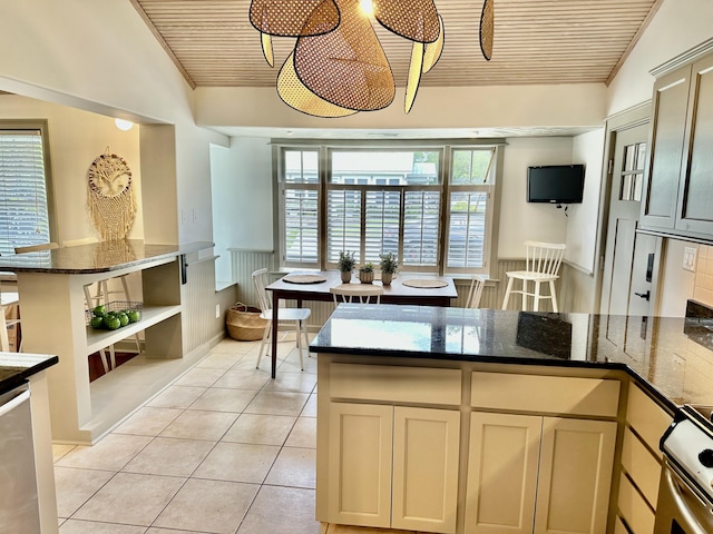 kitchen featuring vaulted ceiling, stainless steel range with electric cooktop, light tile patterned floors, cream cabinetry, and dark stone counters