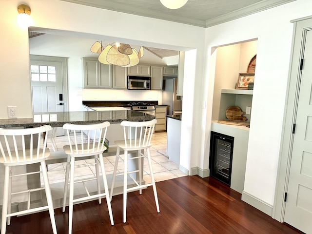 kitchen with gray cabinets, kitchen peninsula, a kitchen bar, crown molding, and appliances with stainless steel finishes