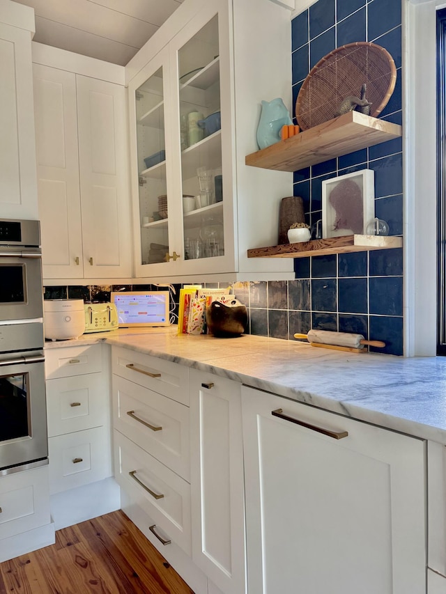 kitchen with white cabinets, double oven, light stone counters, and hardwood / wood-style flooring