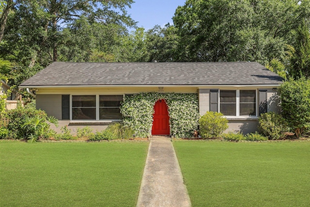 view of front of property featuring a front yard, a shingled roof, and concrete block siding