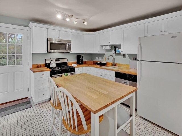 kitchen with wood counters, stainless steel appliances, a sink, light tile patterned floors, and white cabinetry