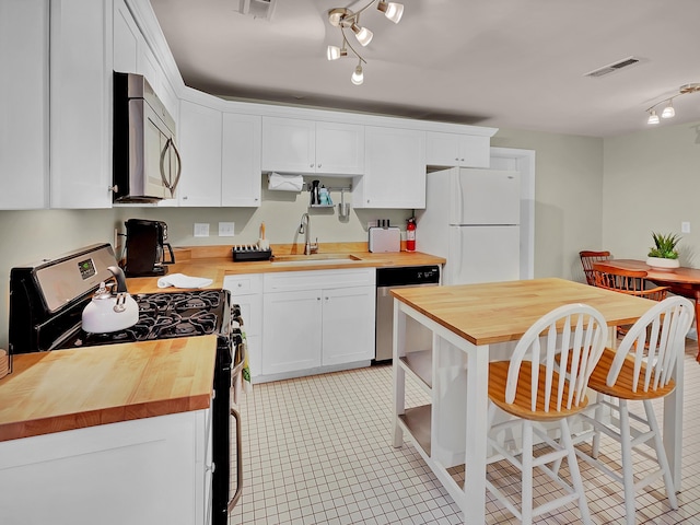 kitchen featuring wood counters, stainless steel appliances, a sink, rail lighting, and white cabinetry