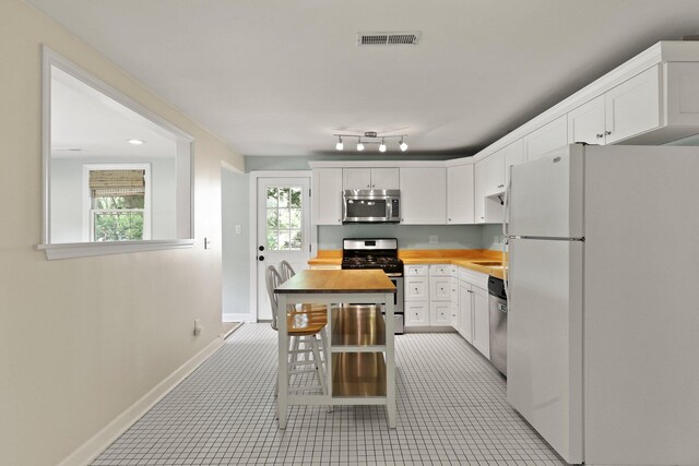 kitchen with appliances with stainless steel finishes, white cabinets, baseboards, wooden counters, and light tile patterned floors
