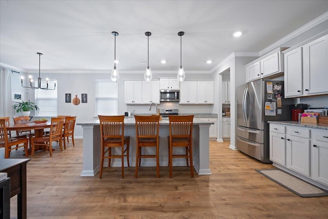 kitchen featuring a breakfast bar area, wood finished floors, ornamental molding, appliances with stainless steel finishes, and white cabinetry