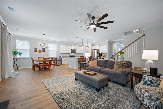 living room with light wood-type flooring, ceiling fan with notable chandelier, visible vents, and ornamental molding