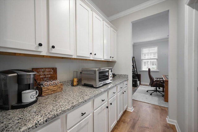 kitchen featuring light stone counters, baseboards, light wood finished floors, white cabinets, and crown molding