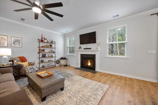 living area featuring visible vents, a fireplace with flush hearth, ornamental molding, and light wood finished floors