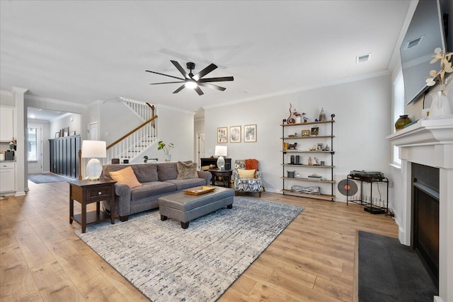 living room featuring visible vents, a fireplace with flush hearth, stairs, and light wood finished floors