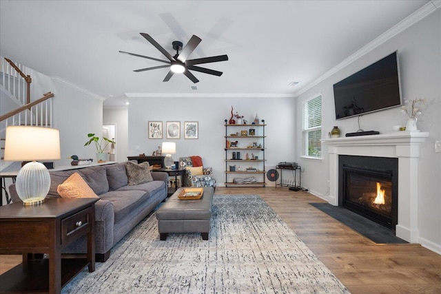 living room featuring wood finished floors, baseboards, a fireplace with flush hearth, ceiling fan, and crown molding