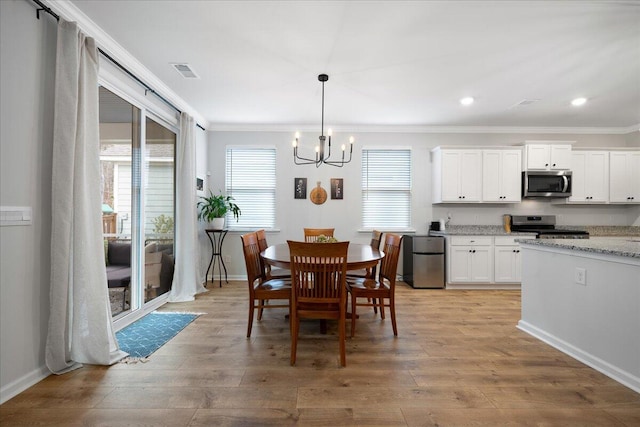 dining area with baseboards, visible vents, an inviting chandelier, ornamental molding, and light wood-type flooring