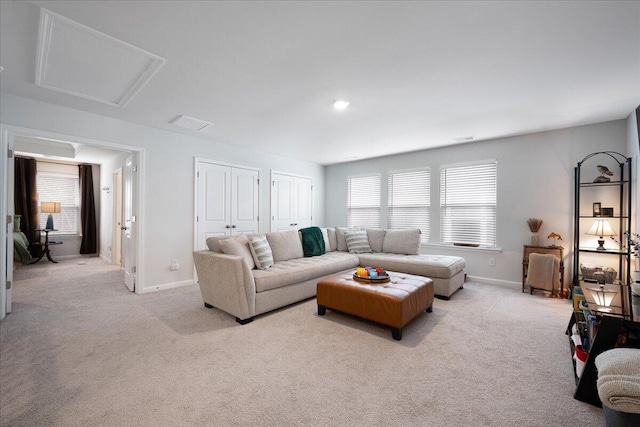 living area with attic access, light colored carpet, and baseboards