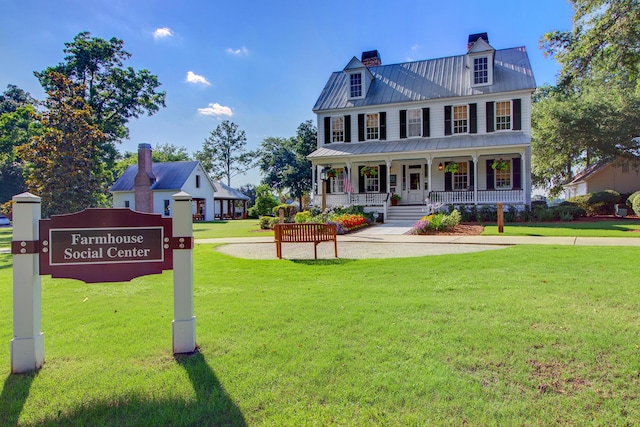 view of front facade featuring a standing seam roof, a porch, a chimney, a front lawn, and metal roof