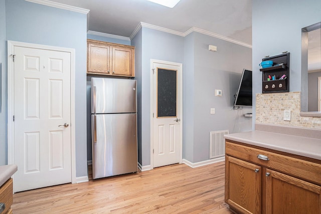 kitchen featuring ornamental molding, light wood-type flooring, stainless steel refrigerator, and decorative backsplash