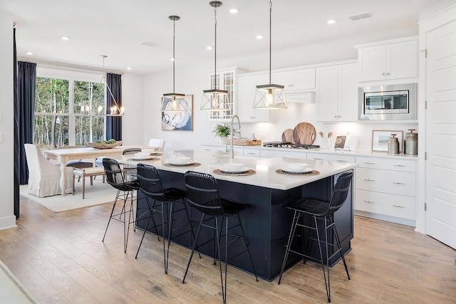 kitchen with appliances with stainless steel finishes, light countertops, an island with sink, and white cabinetry