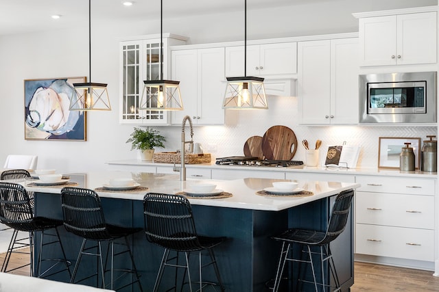 kitchen with a breakfast bar area, white cabinetry, light countertops, appliances with stainless steel finishes, and glass insert cabinets