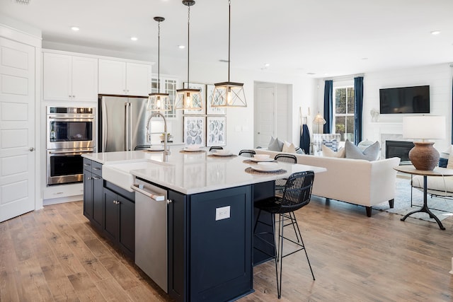 kitchen featuring white cabinets, open floor plan, light countertops, appliances with stainless steel finishes, and a center island with sink