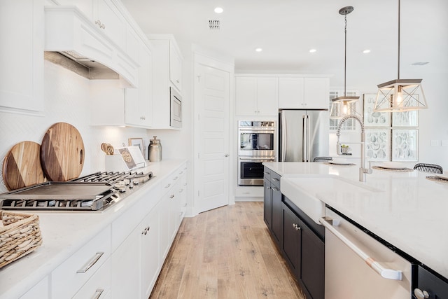 kitchen with hanging light fixtures, white cabinets, stainless steel appliances, and a sink