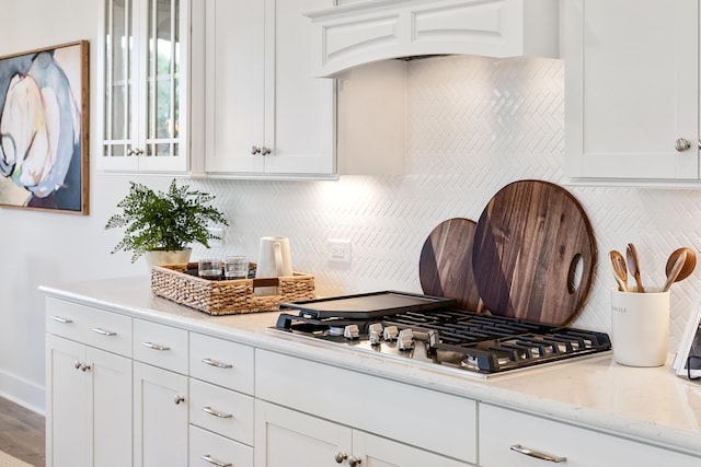 kitchen with tasteful backsplash, stainless steel gas stovetop, glass insert cabinets, white cabinets, and light stone countertops