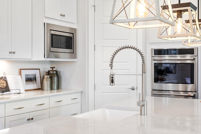 kitchen with stainless steel microwave, white cabinets, and light stone countertops