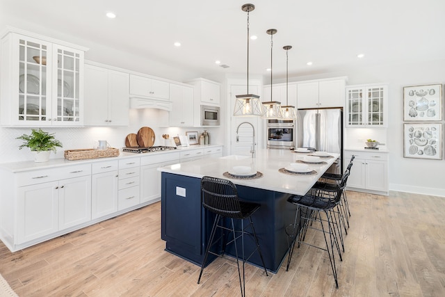 kitchen with a sink, light countertops, a center island with sink, and glass insert cabinets