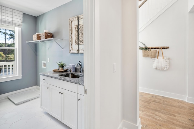 bar featuring light wood-style floors, a sink, and baseboards