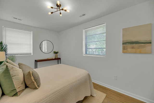 bedroom with a notable chandelier, wood finished floors, visible vents, and baseboards