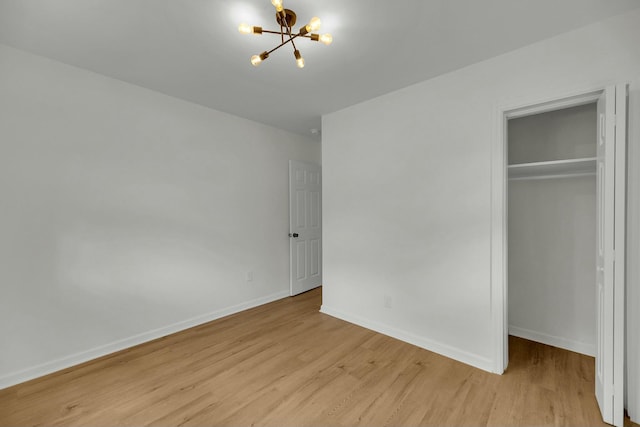 unfurnished bedroom with wood finished floors, a closet, baseboards, a chandelier, and a spacious closet