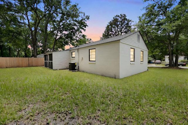 property exterior at dusk with central air condition unit, fence, and a lawn