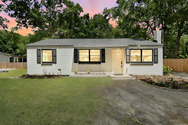 ranch-style home with a lawn, roof with shingles, a chimney, and fence