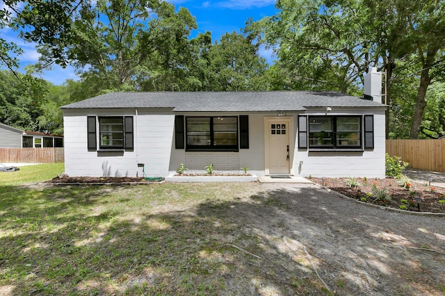 ranch-style home with a chimney, roof with shingles, a front yard, and fence