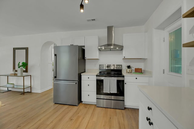 kitchen featuring visible vents, stainless steel appliances, arched walkways, wall chimney exhaust hood, and light countertops