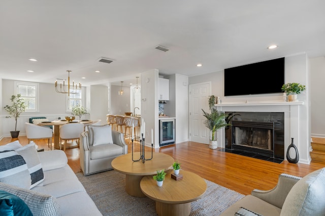 living room featuring light wood-type flooring, a notable chandelier, and beverage cooler