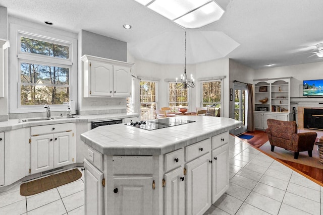 kitchen with black appliances, a sink, a fireplace, light tile patterned floors, and tile counters