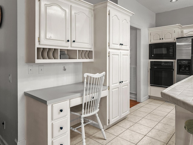 kitchen featuring black appliances, tile counters, built in desk, light tile patterned flooring, and white cabinetry