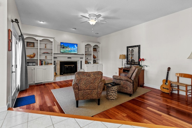 living area featuring ceiling fan, baseboards, wood finished floors, and a fireplace