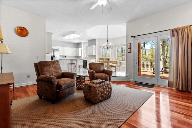 living room featuring ceiling fan with notable chandelier, baseboards, light wood finished floors, and a textured ceiling