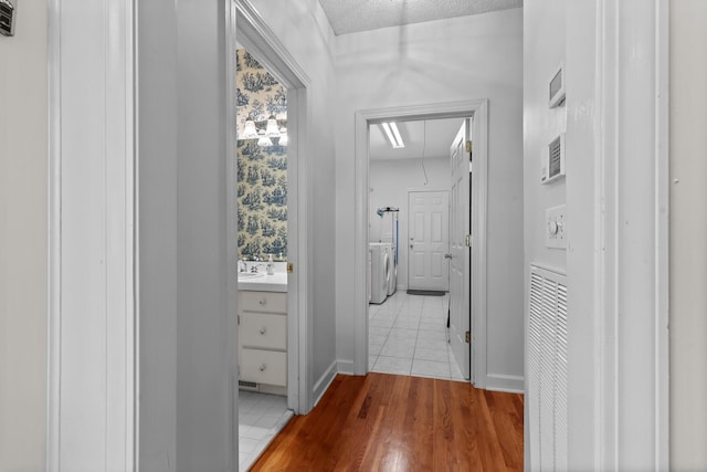 corridor with a textured ceiling, attic access, light wood finished floors, and washing machine and clothes dryer