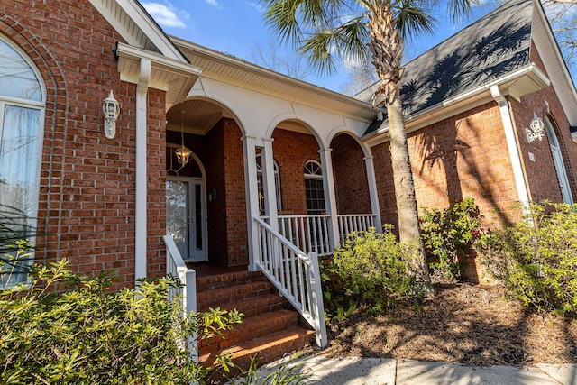 property entrance with a garage, covered porch, brick siding, and a shingled roof