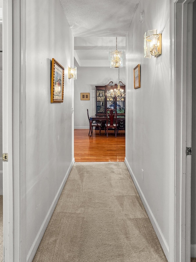 hall featuring a textured ceiling, baseboards, carpet floors, and a chandelier