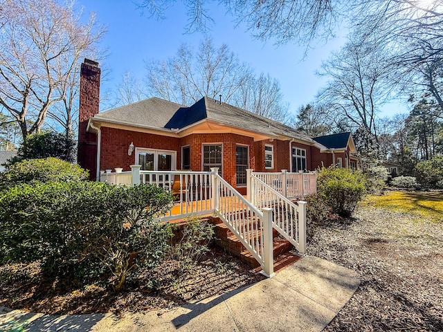 view of front of house with stairs, a wooden deck, brick siding, and a chimney