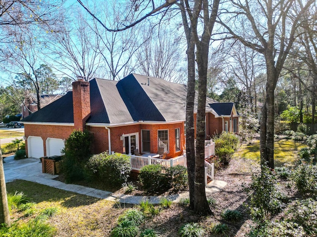 view of home's exterior with a garage, driveway, brick siding, and a chimney