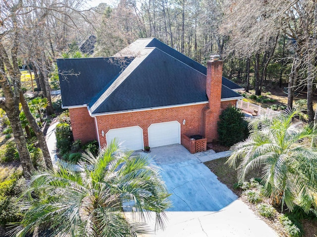 view of side of property featuring brick siding, an attached garage, roof with shingles, a chimney, and driveway