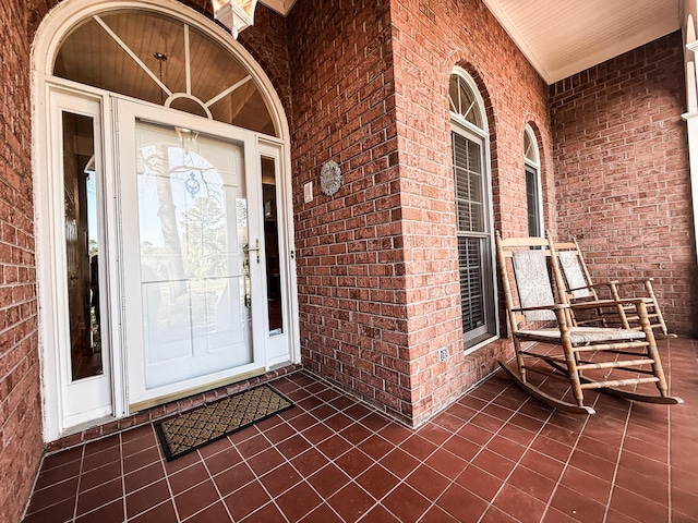 view of exterior entry featuring brick siding and a porch